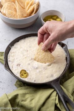 a person dipping tortilla chips into a skillet filled with quesadilla dip