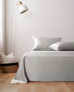 a bed with white sheets and pillows on top of it next to a floor lamp