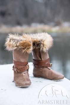 a pair of brown boots with fur on the top and bottom, sitting in front of a body of water