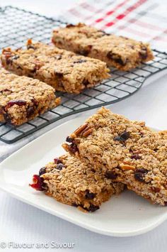 homemade granola bars stacked on a white plate next to a cooling rack with more granola bars in the background