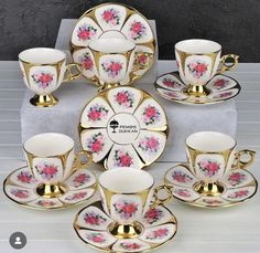 a set of tea cups and saucers with pink flowers on gold trimmings