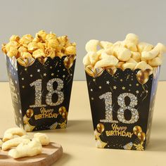 two black and gold birthday popcorn boxes filled with marshmallows on a table