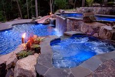 an outdoor hot tub surrounded by rocks and water features a waterfall in the middle with lights on it