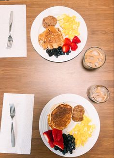 two white plates topped with pancakes and fruit next to silverware on a wooden table