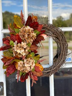 a wreath is hanging on the front door with autumn leaves and hydrangeas around it