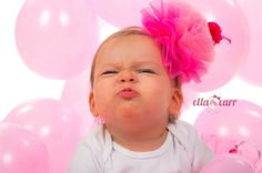 a baby is sitting in front of pink balloons with a flower on it's head