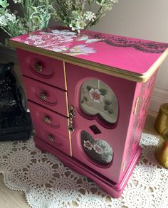 a pink dresser with many drawers and knobs on it's sides, next to a vase with flowers