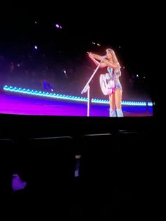 a woman standing on top of a stage in front of a microphone and holding a guitar