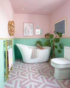 a bathroom with pink and green walls, a white bathtub in the corner and a potted plant next to it