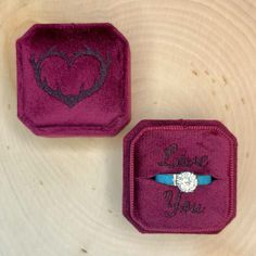 two velvet jewelry boxes with the words love you written on them and a diamond ring in the middle