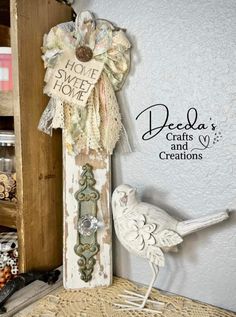 a white bird sitting on top of a table next to a wooden sign that says deeda's crafts and creations