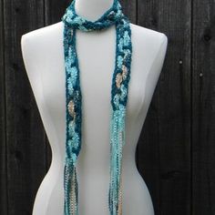 a white mannequin wearing a blue crocheted scarf on top of a wooden table