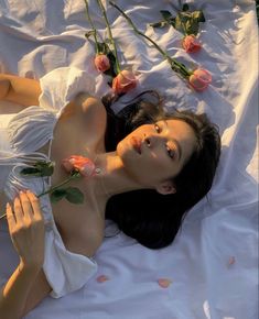 a woman laying on top of a bed with pink roses in her hair and wearing a white dress