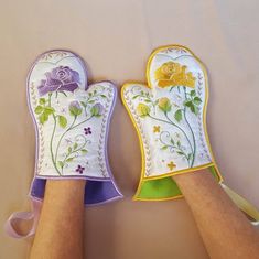 two oven mitts are decorated with flowers and butterflies, one is yellow and the other is purple