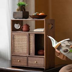 a person reading a book in front of a wooden shelf with baskets and bowls on it