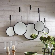 three round mirrors hanging on the wall above a table with flowers in vases and candles