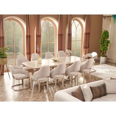 a dining room table surrounded by white chairs and couches in front of large windows