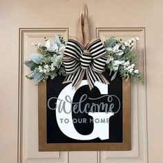 a door hanger with a welcome sign hanging on it's side, decorated with flowers and greenery