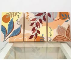 three paintings are displayed on the wall in front of a glass table and white walls