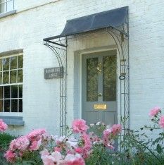 pink flowers in front of a white brick building with a gray door and black awning