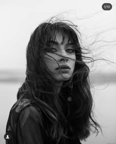 a black and white photo of a woman with her hair blowing in the wind, looking at the camera