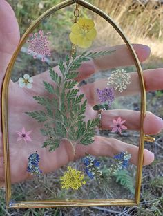 a hand holding a gold frame with flowers in it