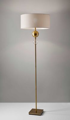 a floor lamp with a white shade on it's base and a gold finish