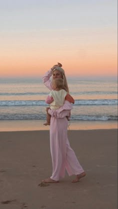 a woman holding a child on the beach at sunset with waves in the back ground