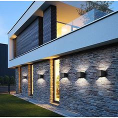 an exterior view of a modern house with stone walls and lights on the outside wall