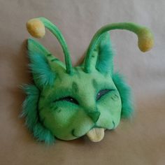 a green cat stuffed animal with yellow eyes and tail sitting on top of a bed