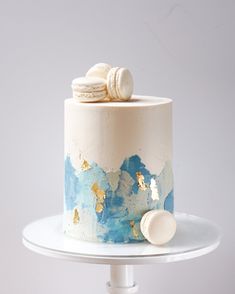 a white cake with blue and gold icing on a plate next to a cookie