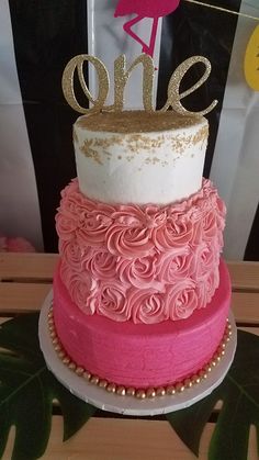 a three tiered cake decorated with pink and gold icing, topped with a flamingo