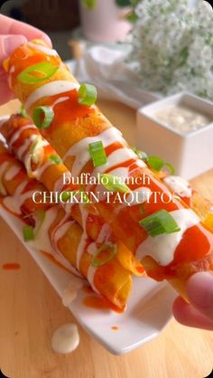 a person is holding up a chicken taco roll with sauce and green onions on it