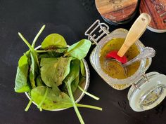 a bowl filled with green vegetables next to two wooden spoons on top of a table