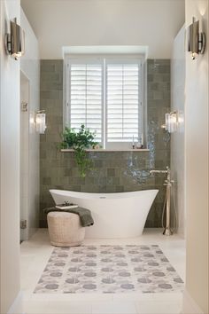 a white bath tub sitting under a window next to a plant in a vase on top of a tiled floor