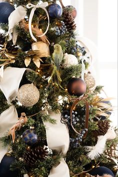 a christmas tree decorated with blue and gold ornaments, bows, pine cones and ribbons