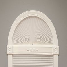 an arched window with white shutters in front of a gray wall