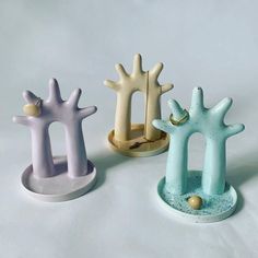 three different colored ceramic objects sitting on a white table top, one is shaped like an arch and the other is shaped like a tree