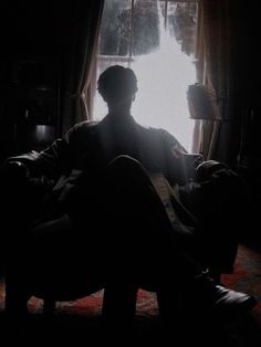 a man sitting on a couch in front of a window with the sun shining through it