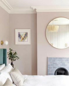 a white bed sitting under a round mirror in a bedroom next to a fire place