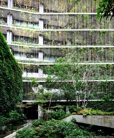 an office building with many plants growing on the outside wall and trees in the front