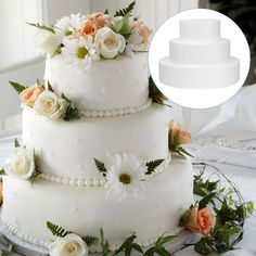 a three tiered white wedding cake with flowers on the top and sides, surrounded by greenery