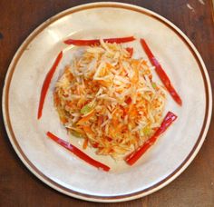 a white plate topped with coleslaw slaw and red peppers on top of a wooden table