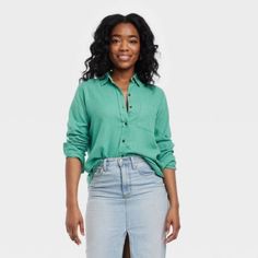 a woman standing in front of a white background wearing a green shirt and jeans with her hands on her hips