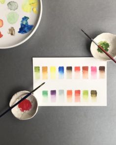 two bowls with paint and some brushes next to them on a gray surface, one bowl has watercolors in it