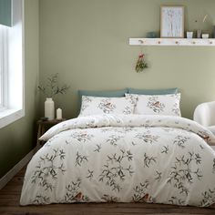 a bed with white comforter and pillows in a green room next to a window