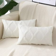 two white pillows sitting on top of a couch next to a green potted plant