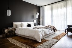 a large white bed sitting on top of a wooden floor next to a tall window