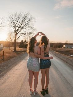 two young women standing in the middle of a road making a heart shape with their hands