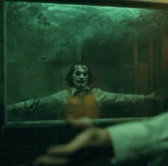 the joker is looking at his reflection in the mirror as he holds out his hand